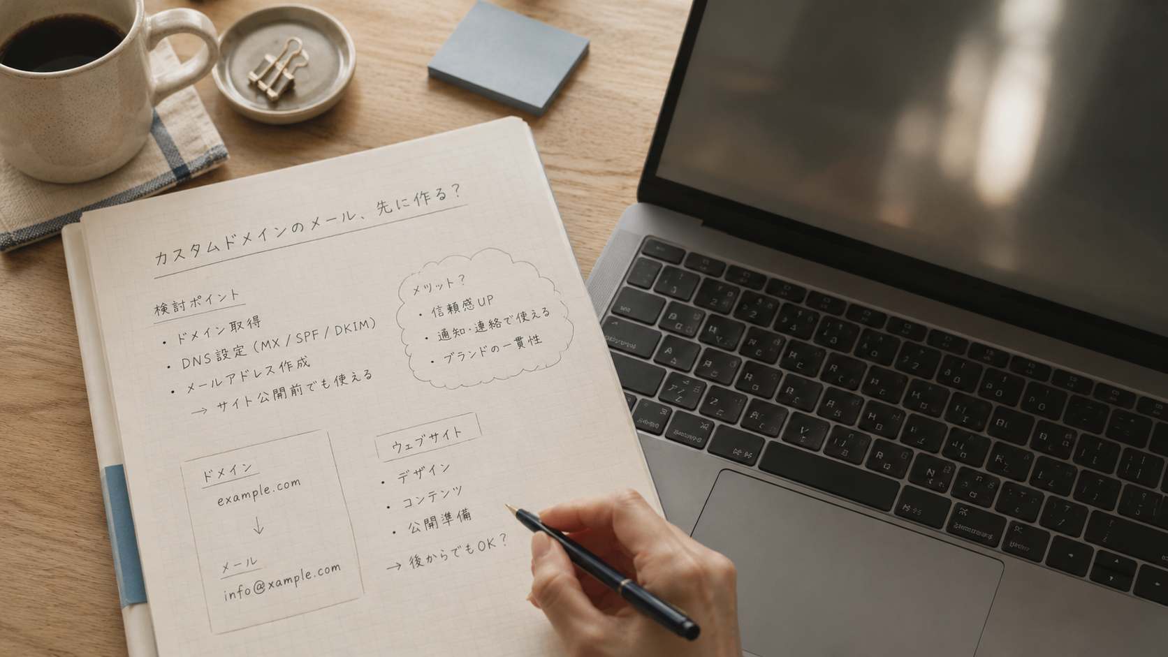 ノートパソコンと紙のメモを並べて独自ドメインメールを検討している手元