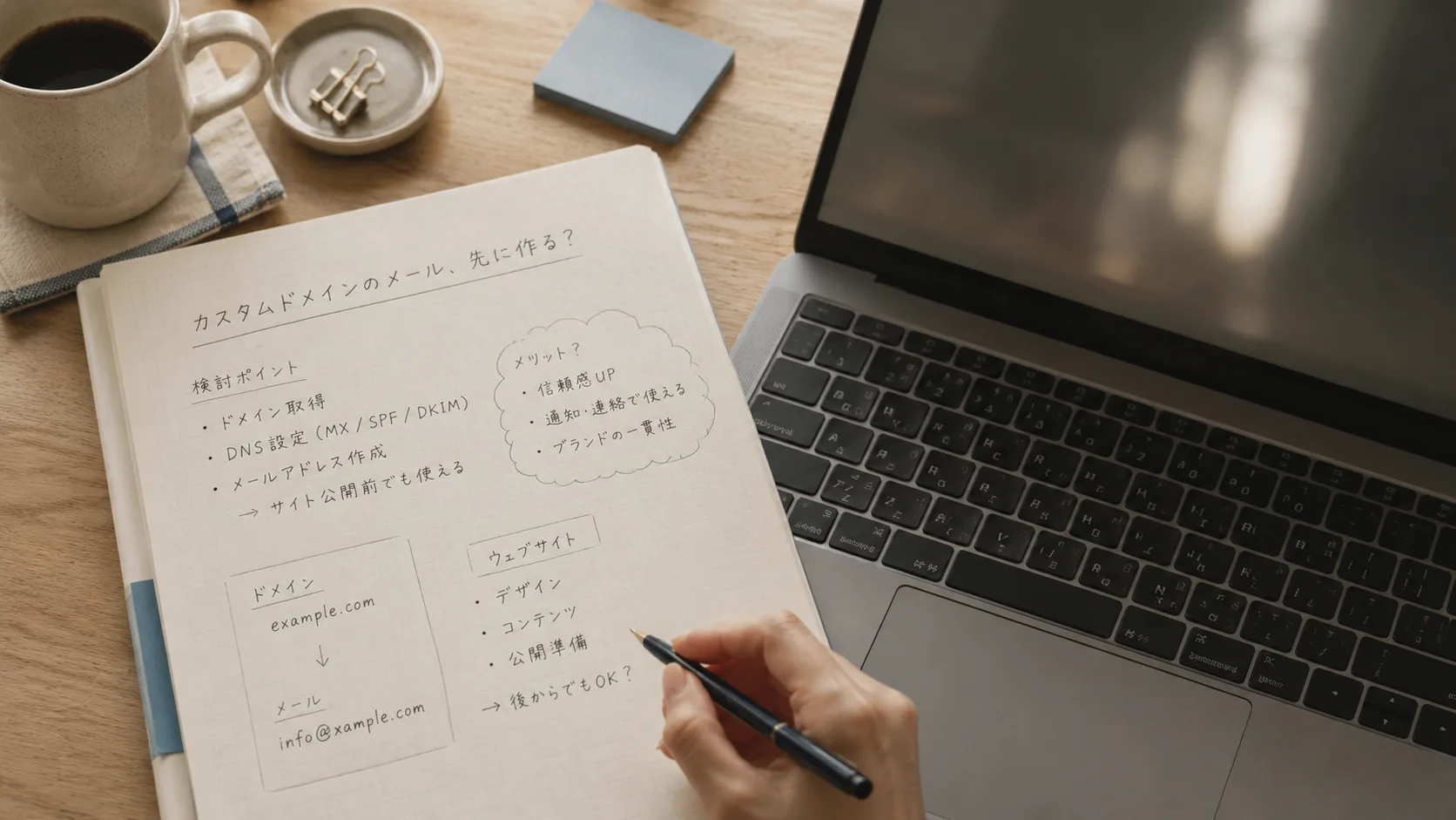 ノートパソコンと紙のメモを並べて独自ドメインメールを検討している手元